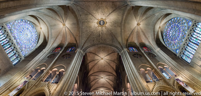 Symmetrical upward view of rib vaults and large rose windows on opposing sides of the transept.