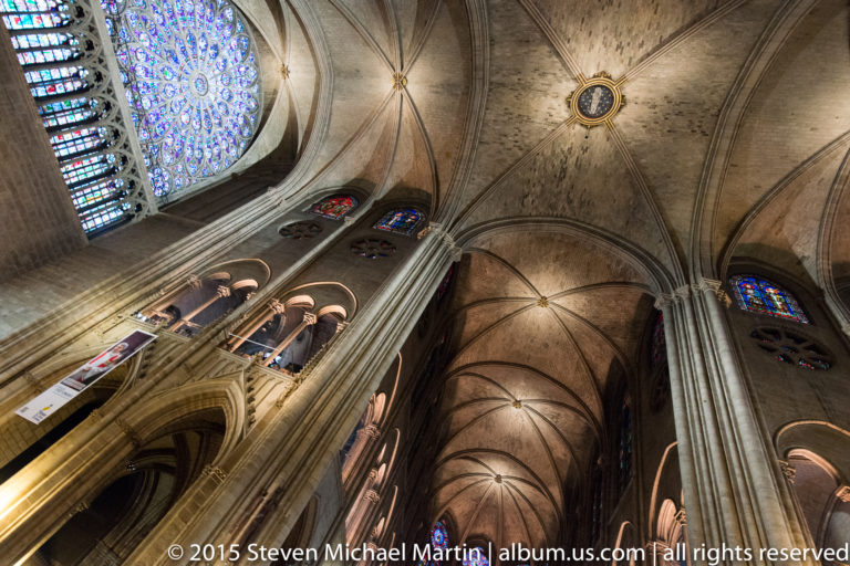 Steep upward view of clustered columns, rib vaults, rose glass, and smaller stained-glass windows.