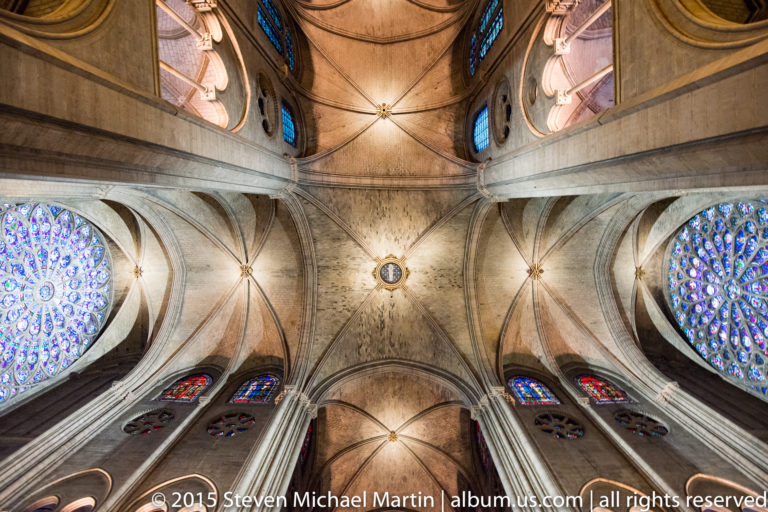 Upward view of rib vaults, clustered columns, and large rose windows on both sides of the cathedral transept.