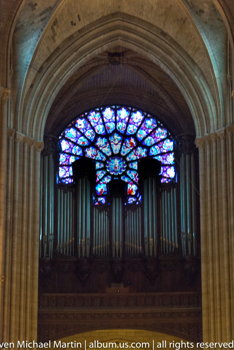 Large pipe organ centered beneath a broad multicolored stained-glass window inside the cathedral.