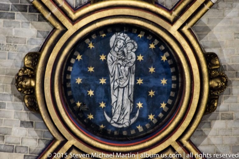 Circular Virgin and Child image on a blue star-filled field within broad gilded moldings.