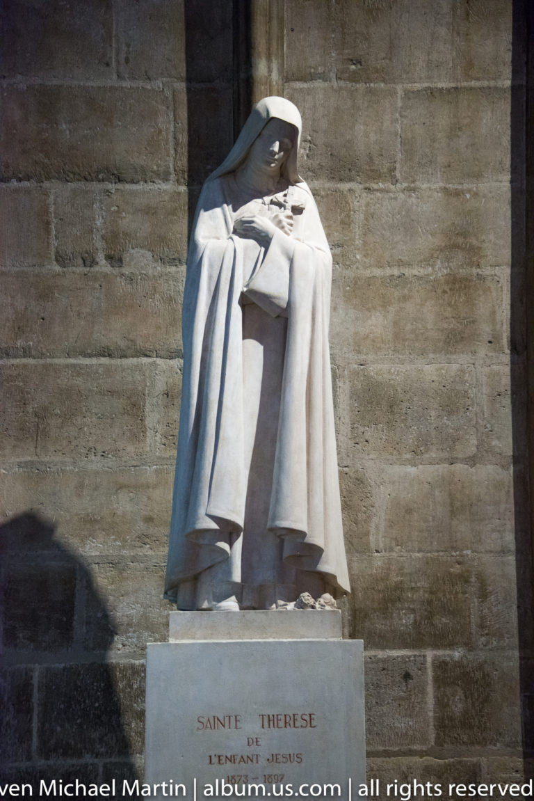 Statue of Saint Thérèse of the Child Jesus in a religious habit, holding devotional attributes on an inscribed pedestal.