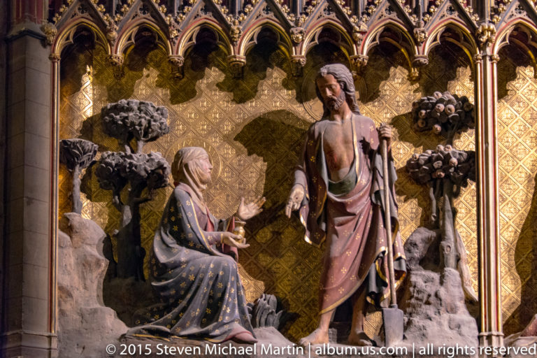 Polychrome choir-enclosure sculpture of Christ appearing to Mary Magdalene among stylized garden trees.