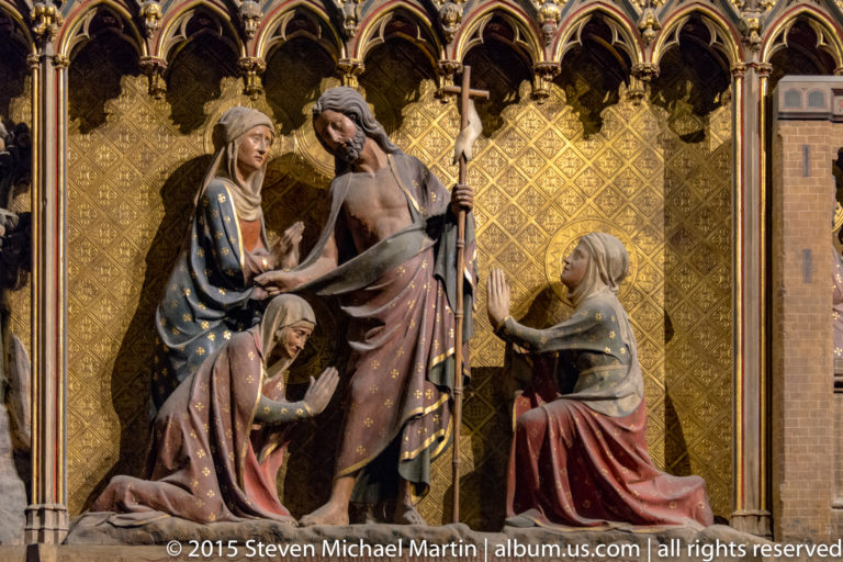 Christ holding a staff stands with two kneeling women and another figure beneath gilded Gothic arches.