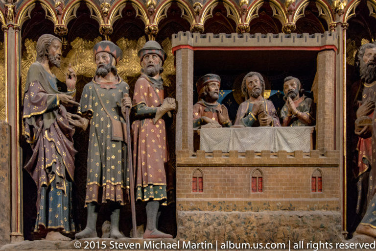 Painted apostles stand beside a crenellated miniature building with additional faces visible through an opening.