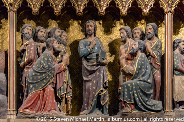Close view of painted apostles gesturing beneath Gothic arches against a gilded patterned background.