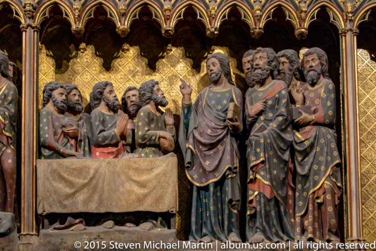 Christ and apostles in painted medieval sculpture beneath gilded pointed arches.