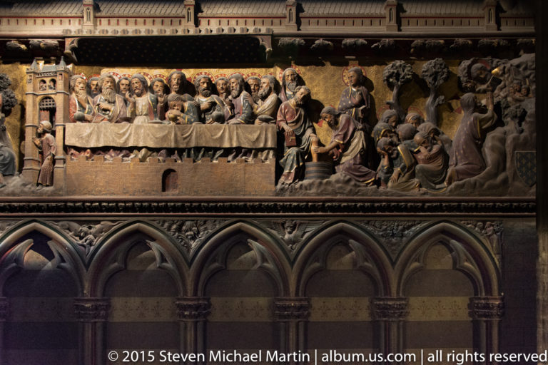 Polychrome relief with Christ and apostles at a table, surrounded by additional sculpted biblical scenes.