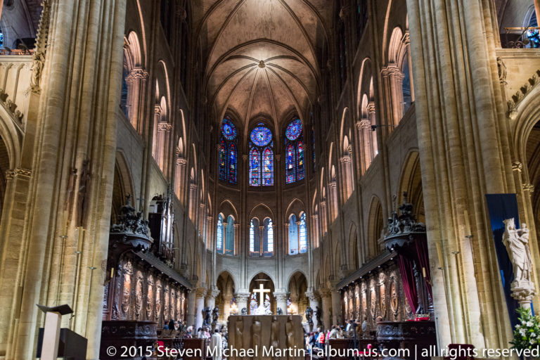 Long interior view toward the choir and apse with stained glass, altar cross, columns, and sculpted choir screens.