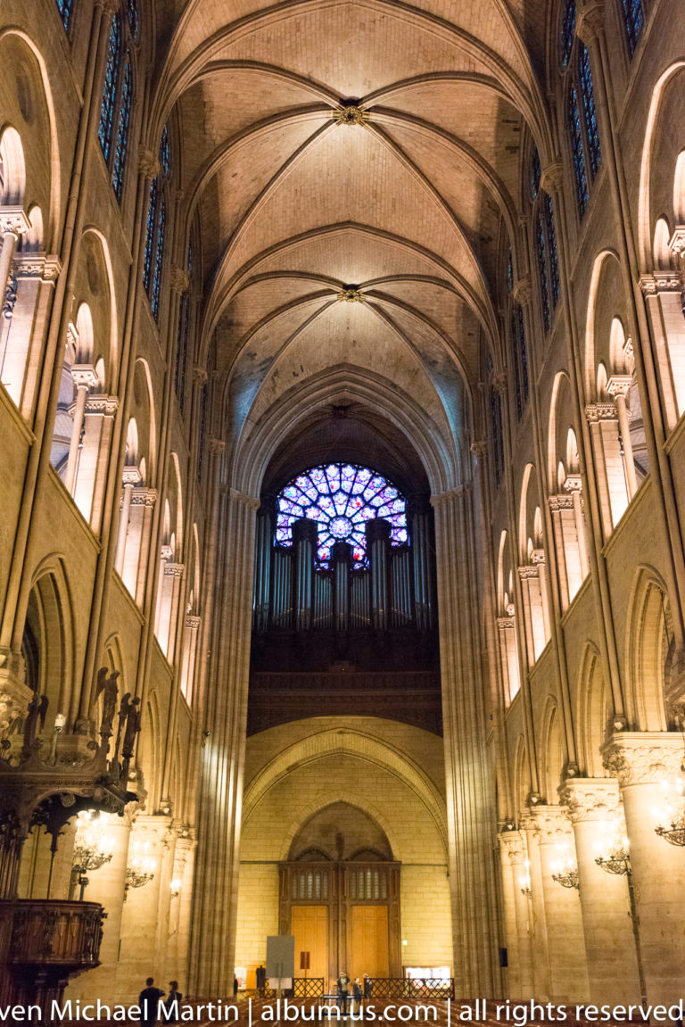 West interior with dark organ loft beneath a stained-glass rose window, framed by tall Gothic arches.