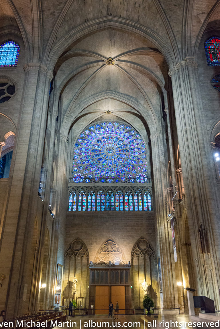 Large circular west rose window above smaller stained-glass openings and the organ loft between massive stone piers.
