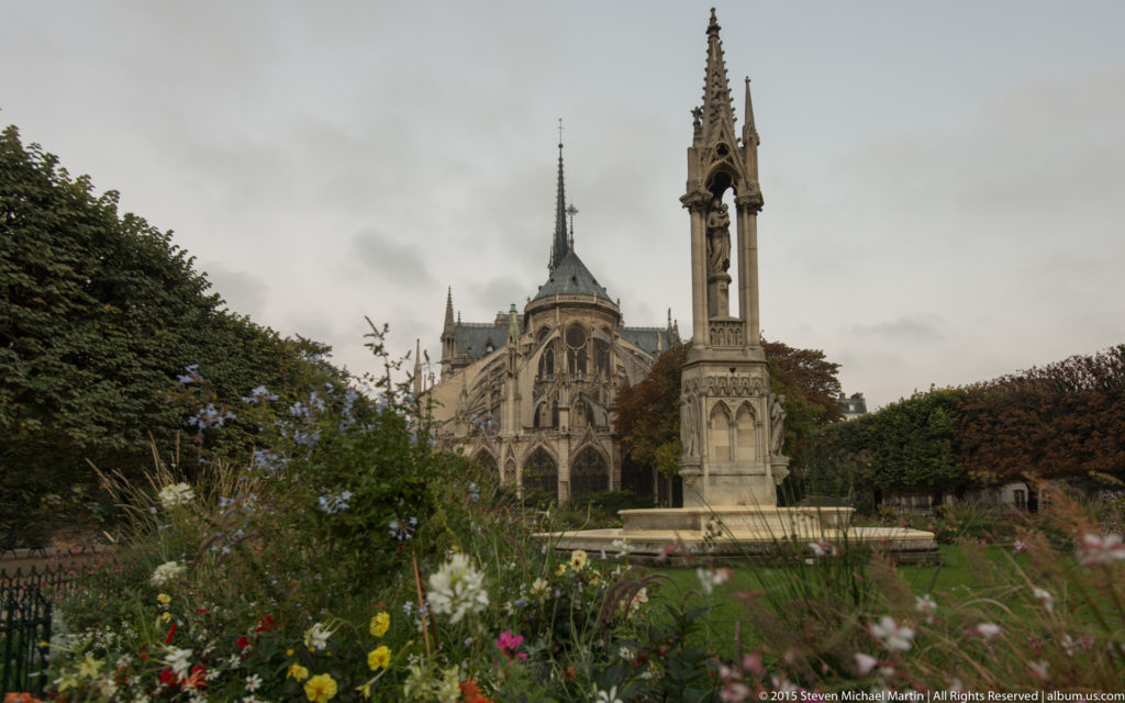 Neo-Gothic Notre-Dame Fountain in a flower garden aligned with the cathedral’s apse and spire.