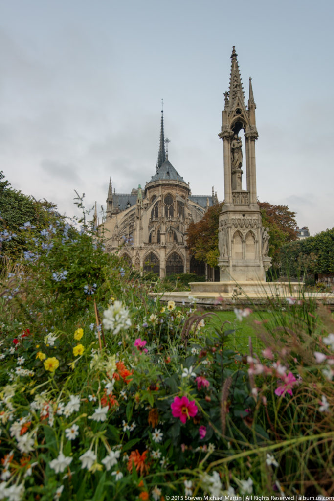 Flower beds around the neo-Gothic Notre-Dame Fountain with the cathedral’s apse and spire behind.