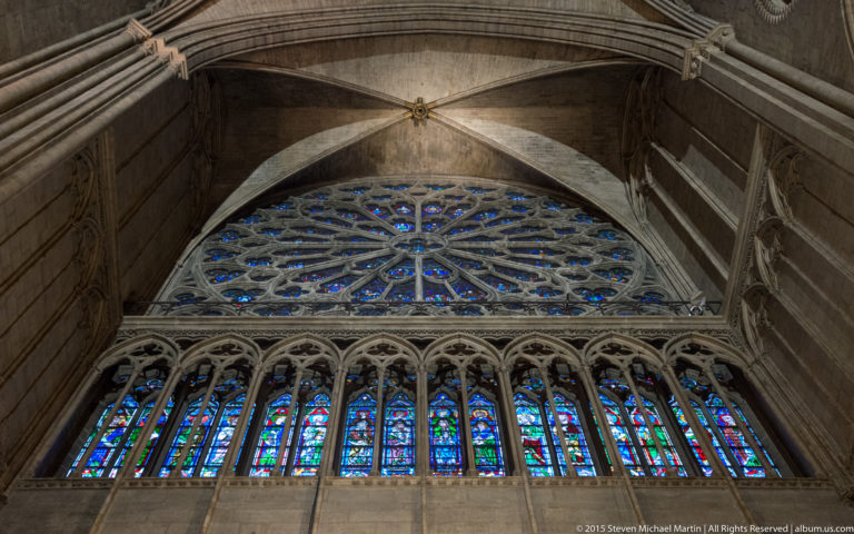 Large rose window above a row of tall stained-glass lancets, framed by stone arches and vaulting.