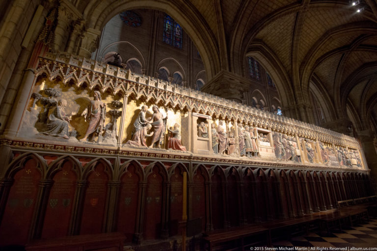 Long polychrome biblical relief sequence above a dark choir enclosure beneath Gothic vaults.
