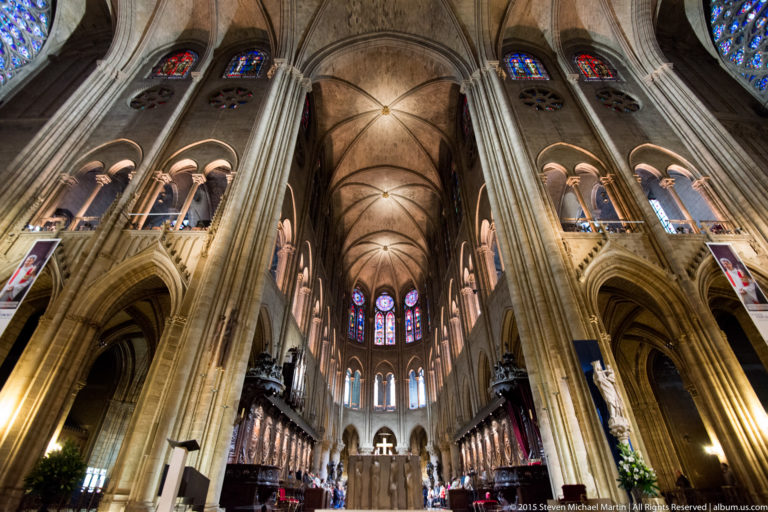Centered interior view toward the altar and apse with stained glass, choir screens, piers, and rib vaults.