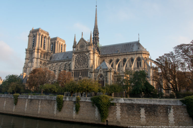 South side of Notre-Dame with transept rose window, flying buttresses, pinnacles, roof, trees, and embankment.