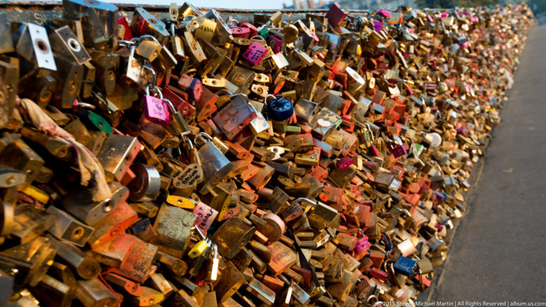 Close view of hundreds of overlapping padlocks attached densely to a metal riverside railing.