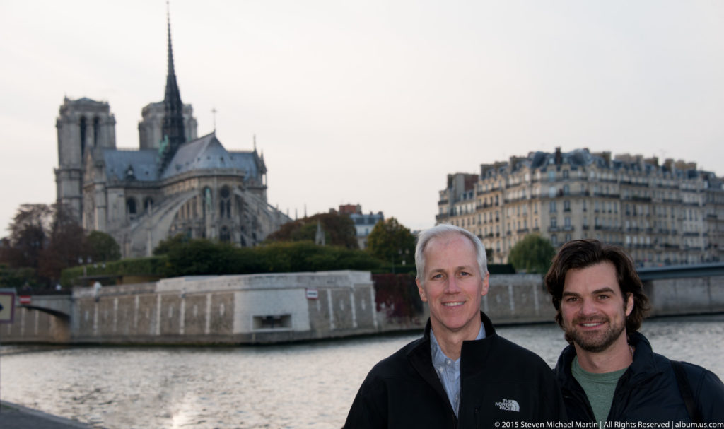 Two men standing beside the Seine with Notre-Dame de Paris softly focused across the river behind them.