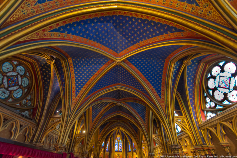 Decorated lower chapel interior of Sainte-Chapelle, with blue fleur-de-lis vaults, gilded ribs, pointed arches, and small stained-glass windows.