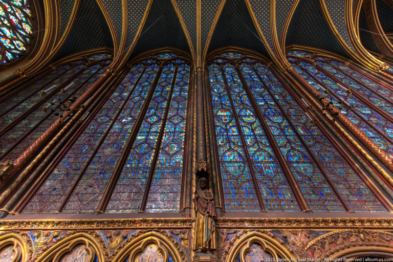 Upper chapel stained-glass lancets and painted architectural framework at Sainte-Chapelle, viewed upward from the lower wall arcade.