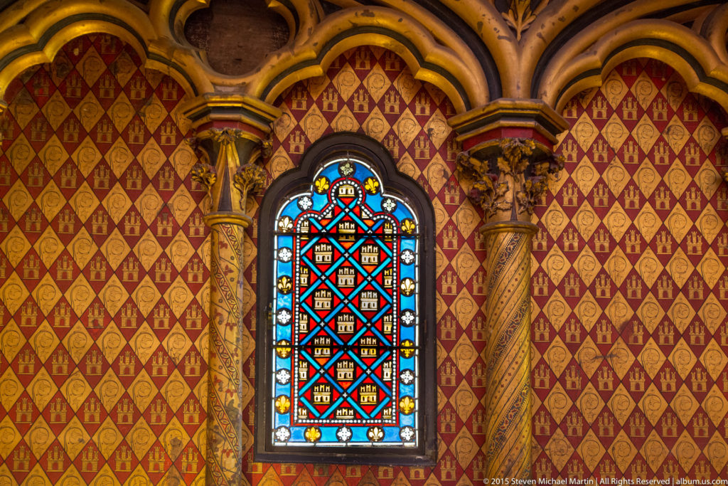 Decorative lower-chapel window at Sainte-Chapelle, surrounded by red-and-gold heraldic wall patterning and carved colonnettes.