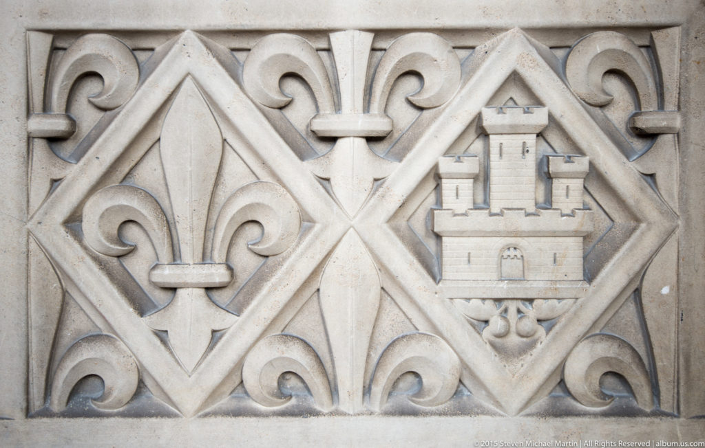 Carved stone balustrade detail near Sainte-Chapelle, patterned with fleurs-de-lis and a crowned castle emblem.