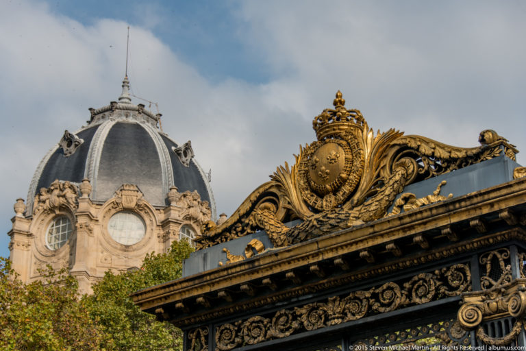 Gilded ornamental cresting in the Palais de Justice complex, with a domed historic building rising behind it near Sainte-Chapelle.