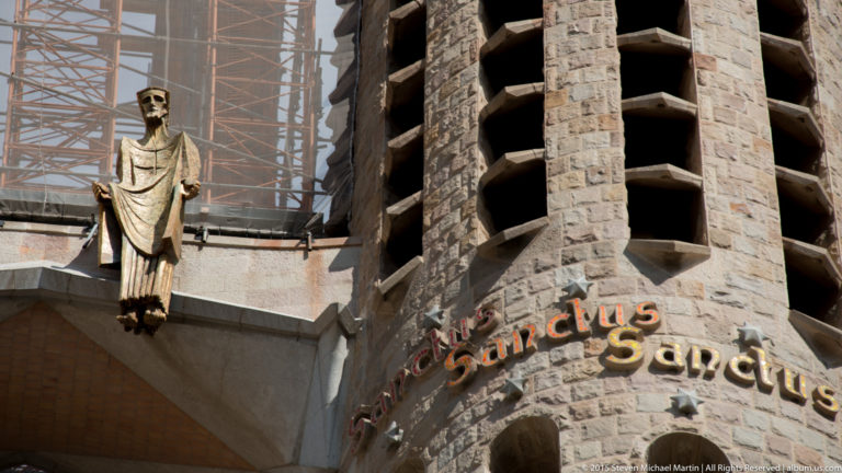 Winged ox sculpture beside the words “Sant Lluc” on a stone wall of the Sagrada Família.