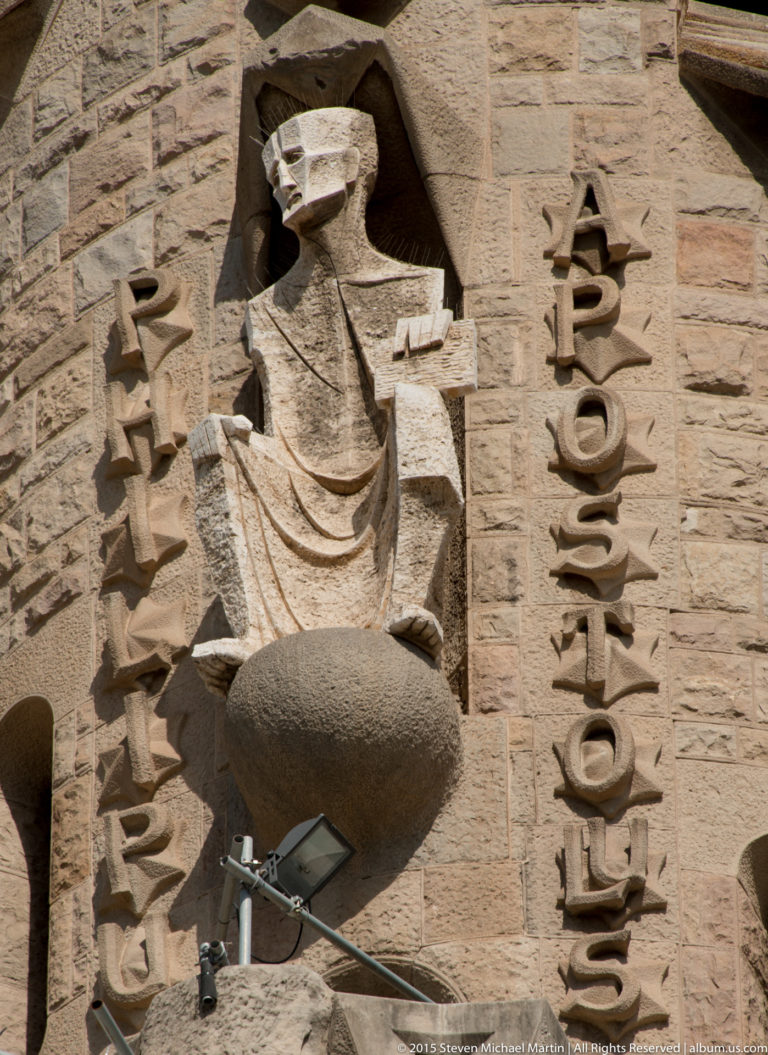 Vertical HOSANNA inscription beside a monumental carved stone figure on the Sagrada Família exterior.