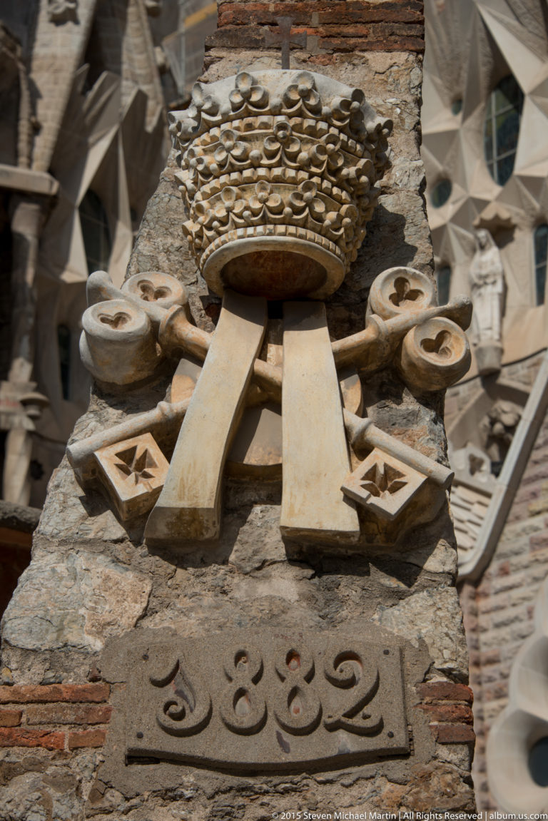 Large stone fruit-cluster ornament above a stem-like support amid carved details on the Sagrada Família exterior.
