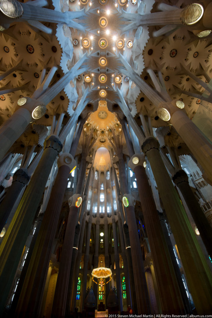 Wide interior view of the Sagrada Família nave with branching columns, luminous patterned ceiling, sanctuary, and stained glass.