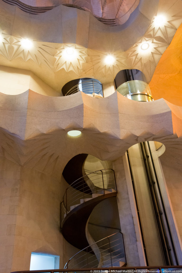 Small spiral staircase beneath curving pale stone galleries and star-like ceiling lights inside the Sagrada Família.