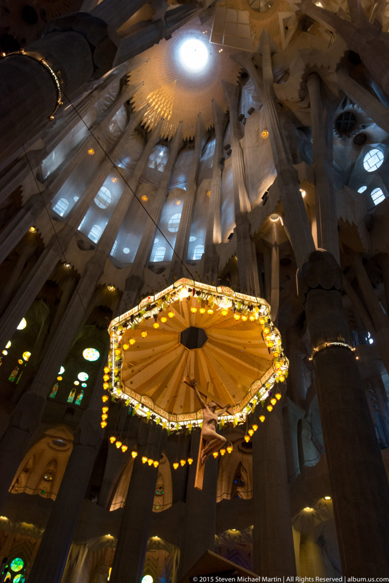 Illuminated circular sanctuary canopy beneath branching columns, vaults, skylights, and stained glass inside the Sagrada Família.