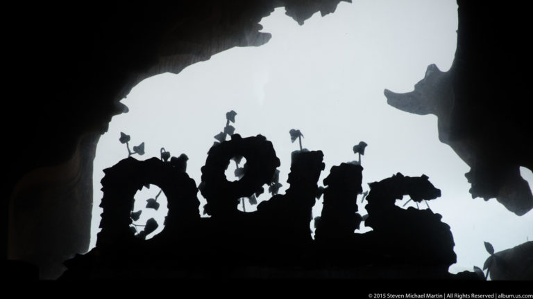 Backlit irregular sculptural letters silhouetted against a bright opening within the Sagrada Família.