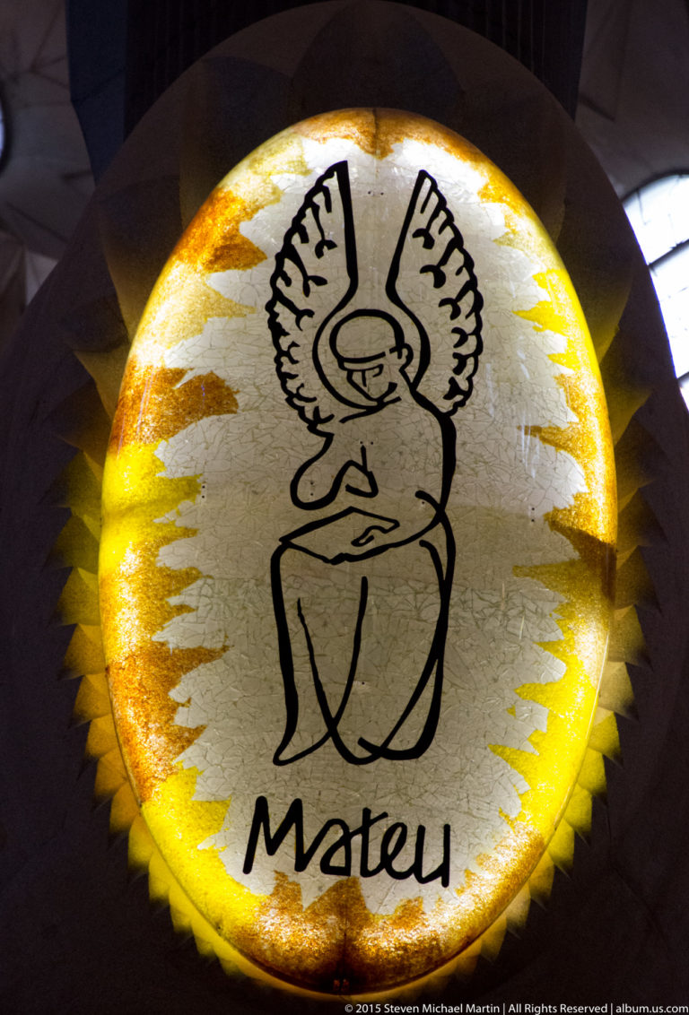 Round yellow-edged medallion with a stylized winged human figure and the name Mateu.