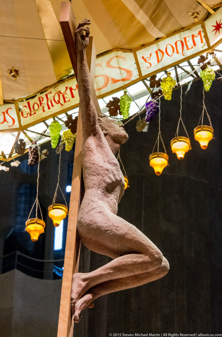 Side detail of Christ on the crucifix beneath an inscribed canopy decorated with grapes and hanging golden lamps.