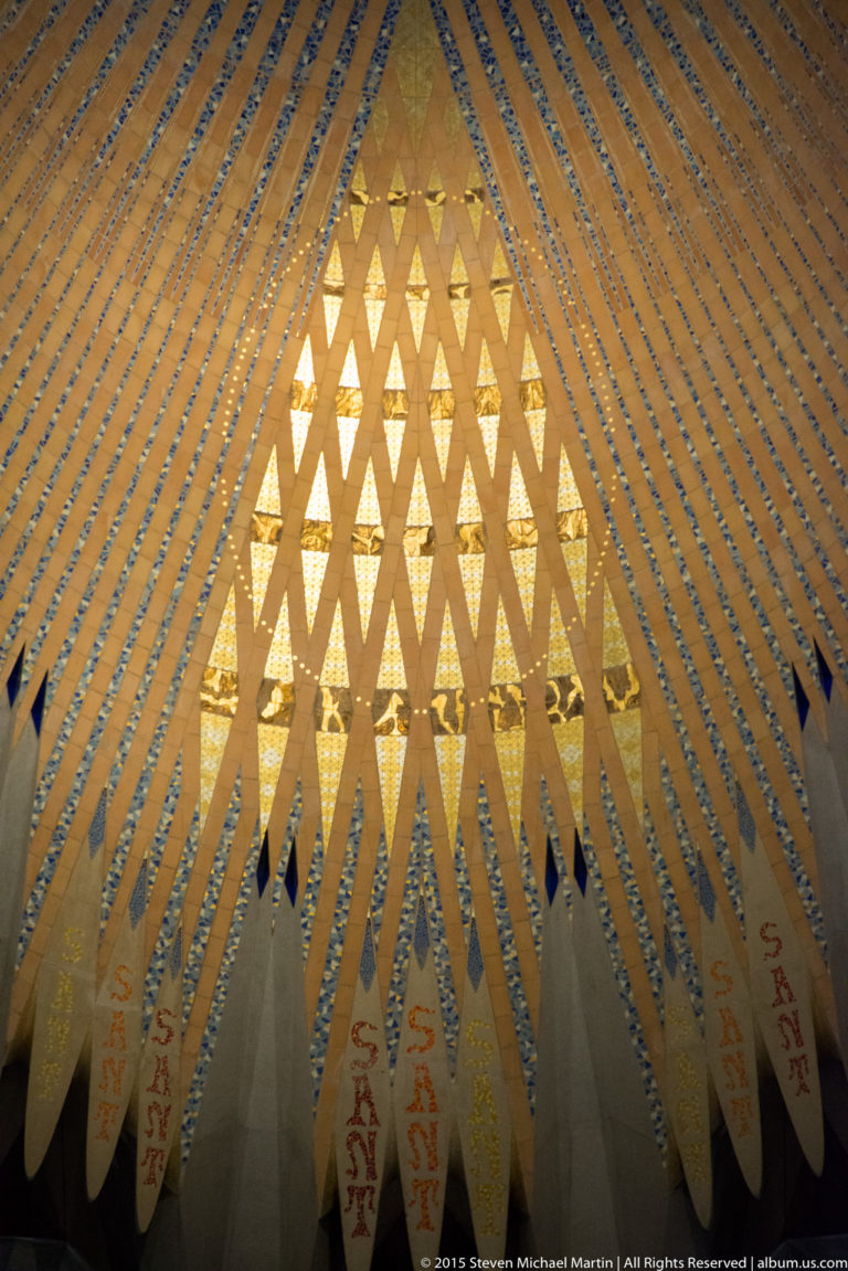 Layered diagonal screen before a glowing triangular pattern of repeated openings inside the Sagrada Família.