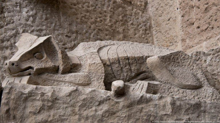 Crouching carved horned animal integrated into rough stonework on the Sagrada Família Passion façade.