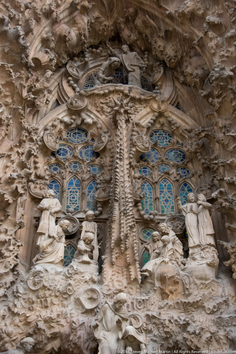 Religious figures, blue-green windows, and dense organic stone ornament on the Sagrada Família Nativity façade.