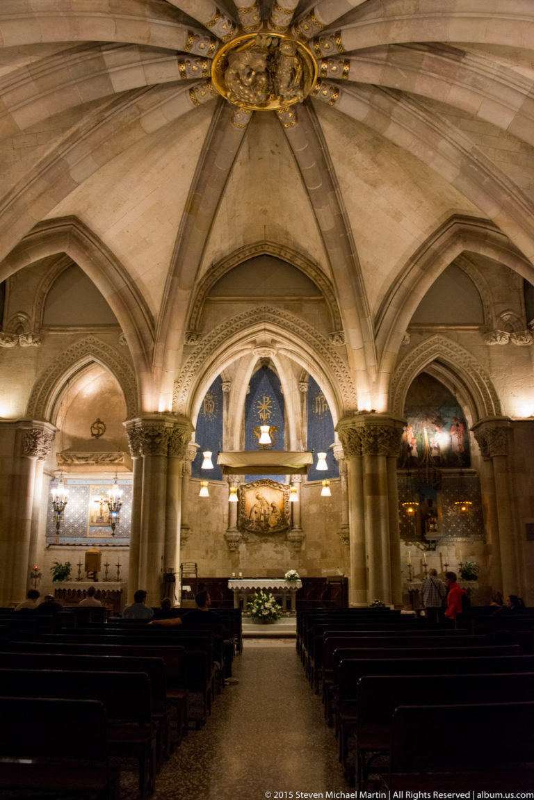 Stone-vaulted chapel interior with rows of pews leading to an altar beneath pointed arches and heavy columns.