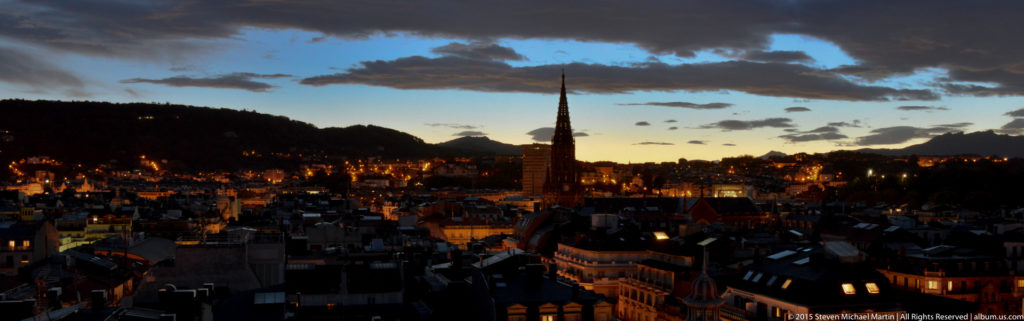 Slender church spire rising above San Sebastián rooftops at dusk beneath broken clouds.