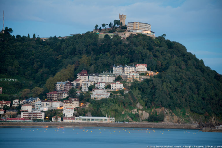 Wooded Monte Urgull rising above waterfront buildings, with fortifications and the Sacred Heart monument near the summit.