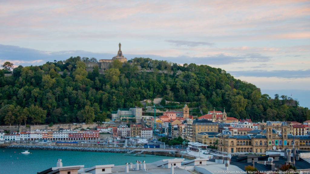 Wooded Monte Urgull with the Sacred Heart monument above waterfront buildings and San Sebastián City Hall.