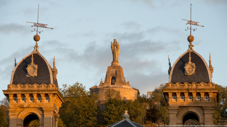Two ornate City Hall roof towers frame the distant Sacred Heart monument on Monte Urgull.