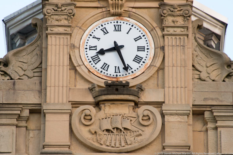 Close architectural detail of San Sebastián City Hall showing a Roman-numeral clock, carved emblem, pilasters, and scrollwork.