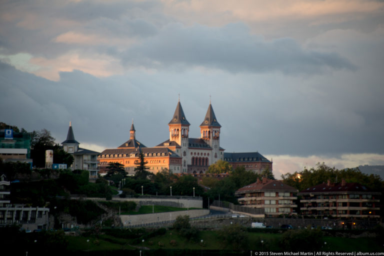 Miramar Palace on a green hillside, with pale walls, red roofs, and multiple pointed towers lit by evening sun.