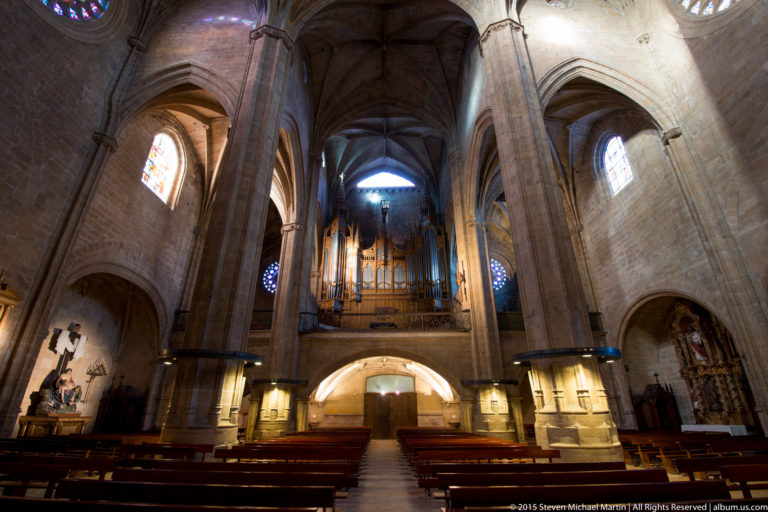 Interior of a Gothic stone church looking toward a large pipe organ above the entrance, framed by tall piers and vaults.