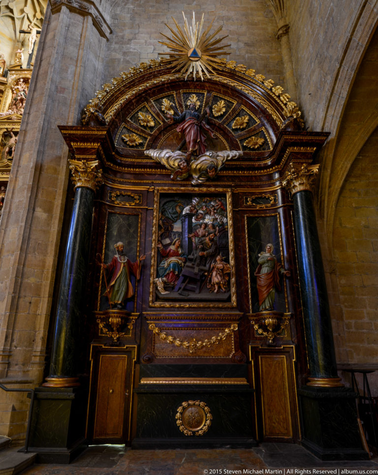 Dark side altarpiece with gilded trim, black columns, several religious paintings, and a radiant sunburst above.