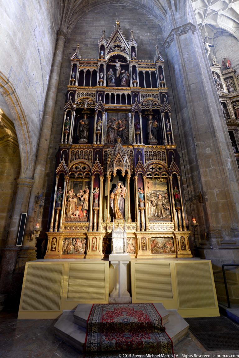 Tall polychrome side-chapel retablo with sculpted figures, relief panels, pinnacles, and gilded architectural ornament.